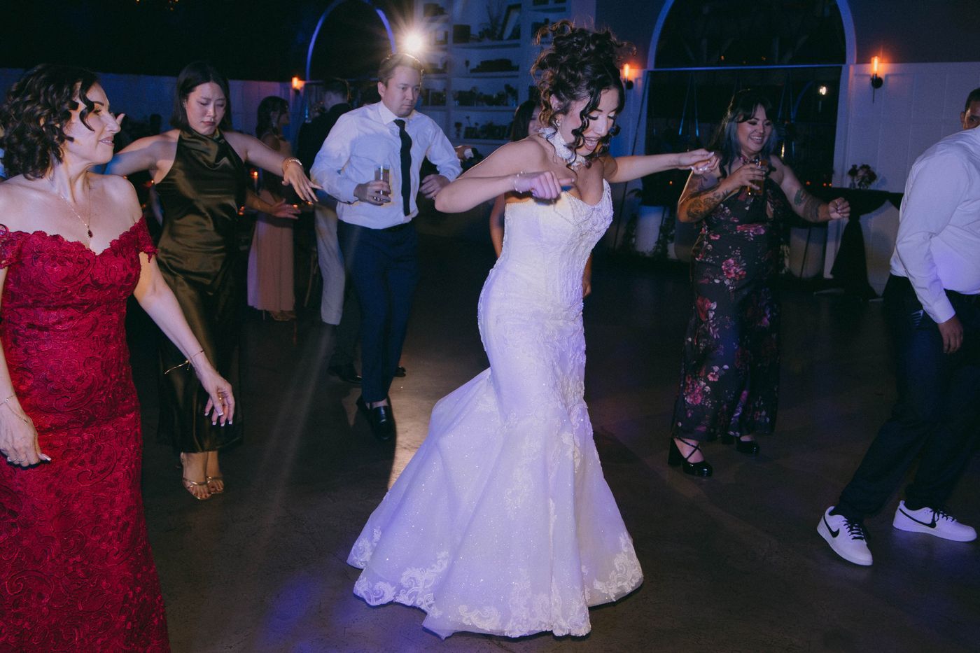 A bride in a white gown dances in the middle of the floor with family and friends of different generations around her